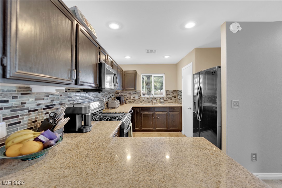 Kitchen with granite peninsula, dark wood cabinets, colorful tile backsplash, and stainless steel appliances.