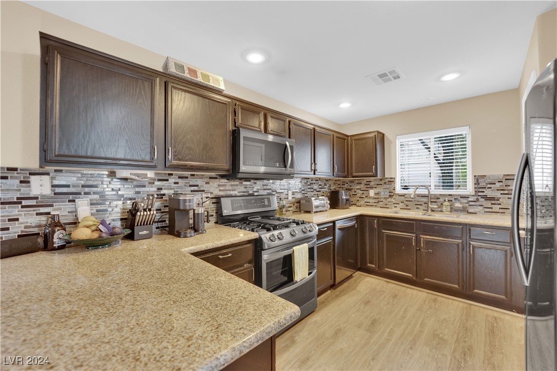 Kitchen with dark wood cabinets, granite counters, a multicolored tile backsplash, and stainless steel appliances.