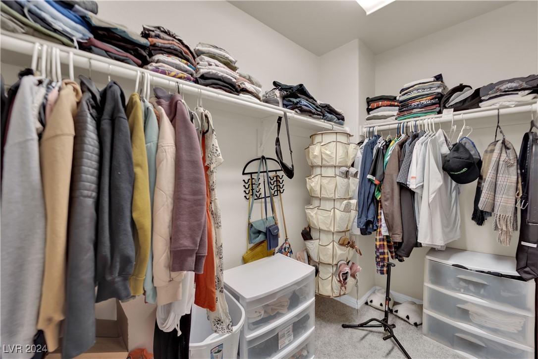 Walk-in closet with clothes on two walls, upper shelves, hanging organizers, and plastic drawer units.