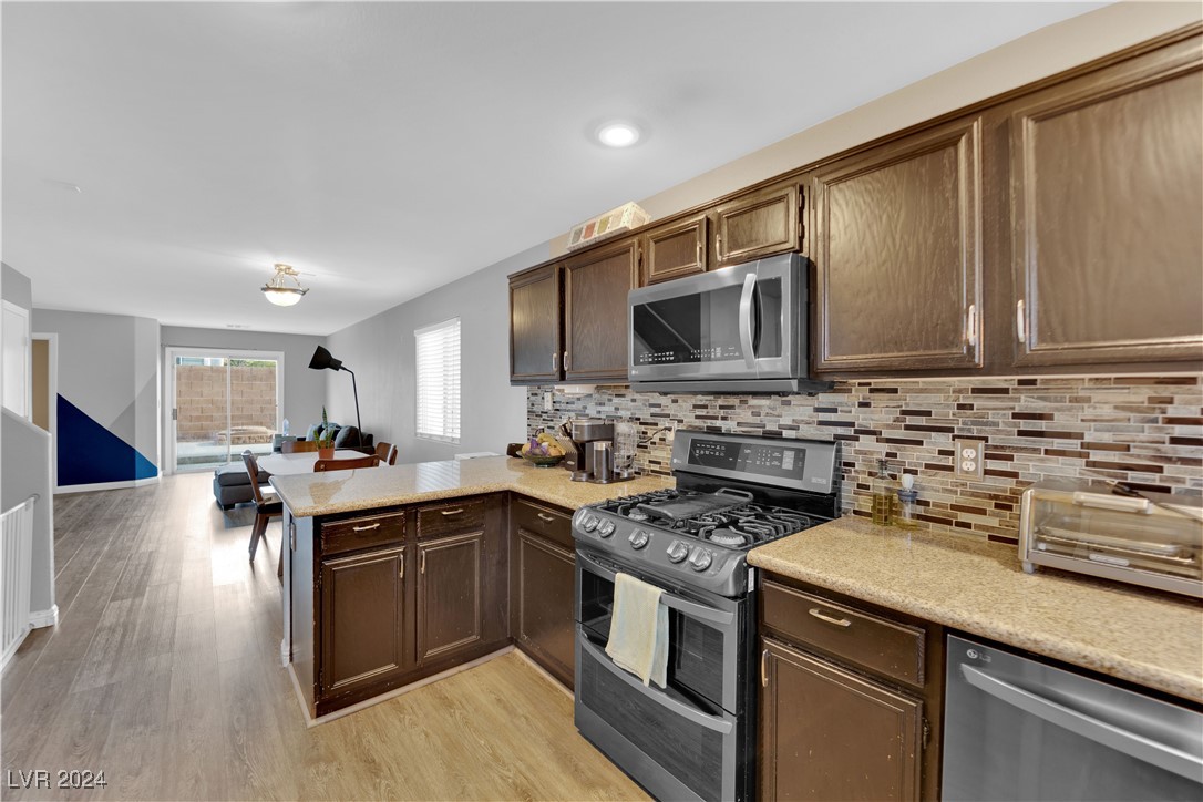 Kitchen with dark wood cabinets, stone counters, mosaic backsplash, and stainless steel appliances.