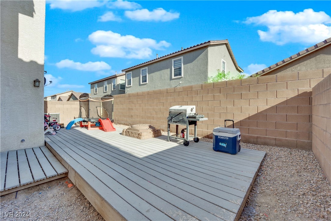 Backyard with a raised gray deck, barbecue grill, children's playset, and block walls.