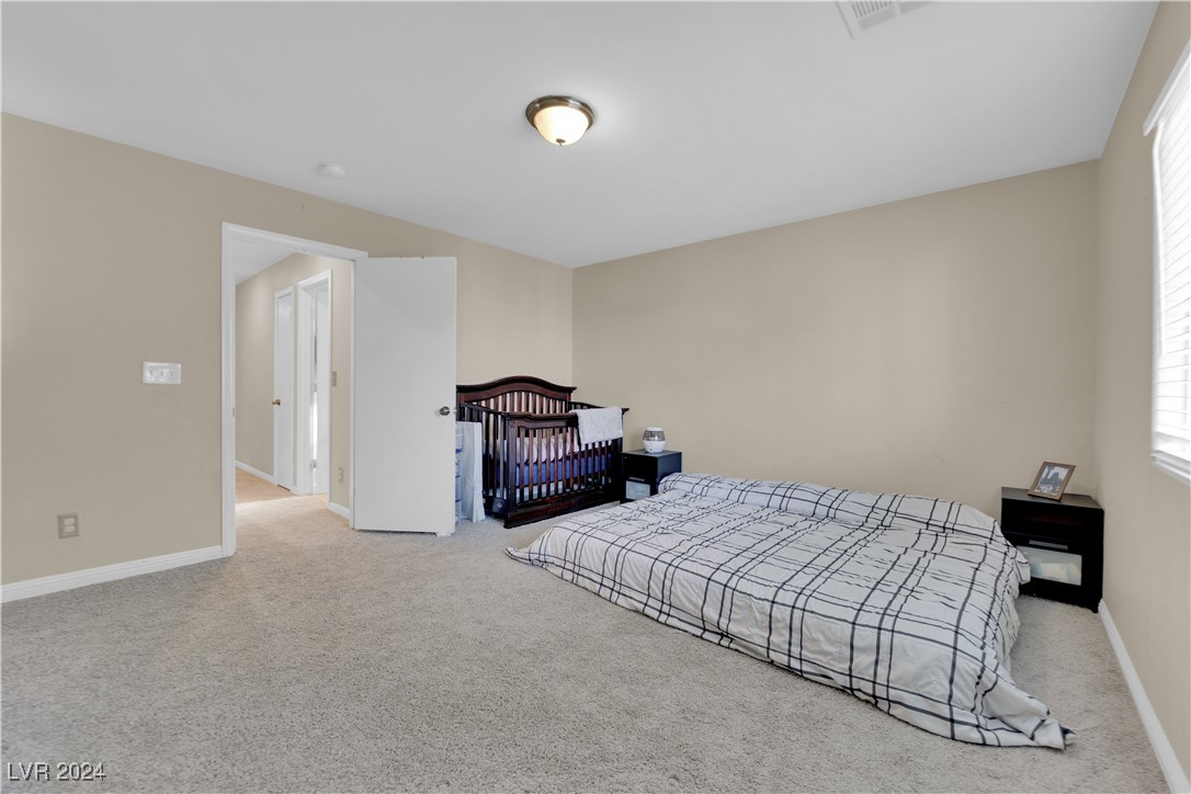 Carpeted bedroom with a low bed and dark wood crib beside an open doorway.