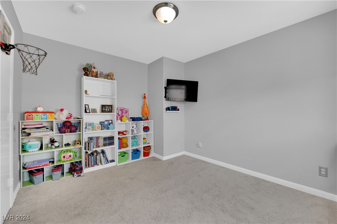 Carpeted playroom with toy-filled shelves, a wall-mounted television, and a small basketball hoop.