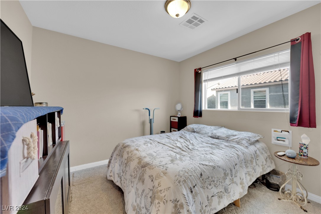 Bedroom with a floral-covered bed, burgundy curtains, and a window overlooking a neighboring home.
