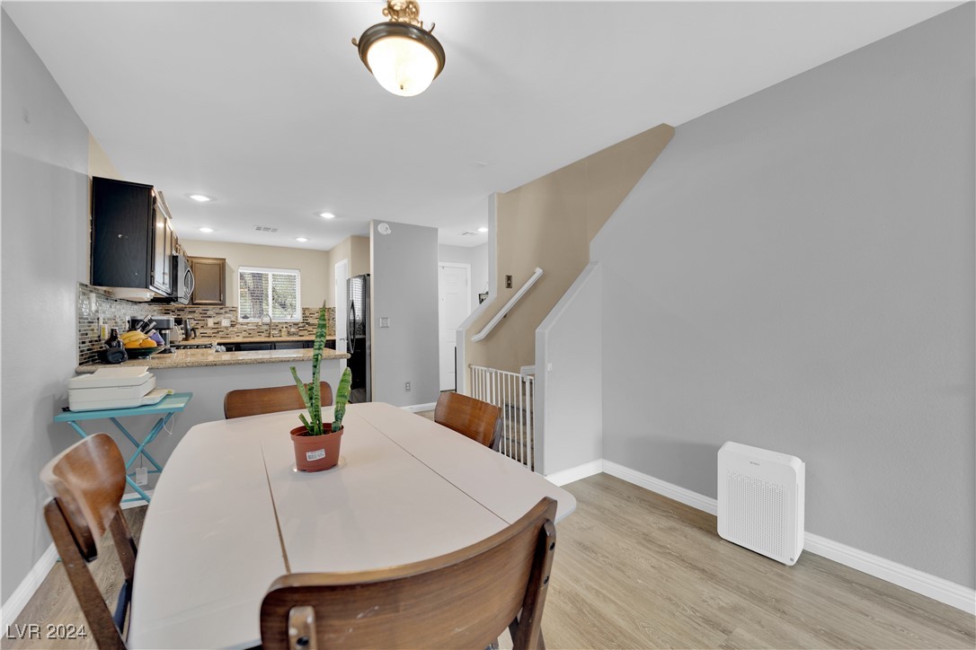 Dining area with a white table and wooden chairs beside the kitchen and staircase.