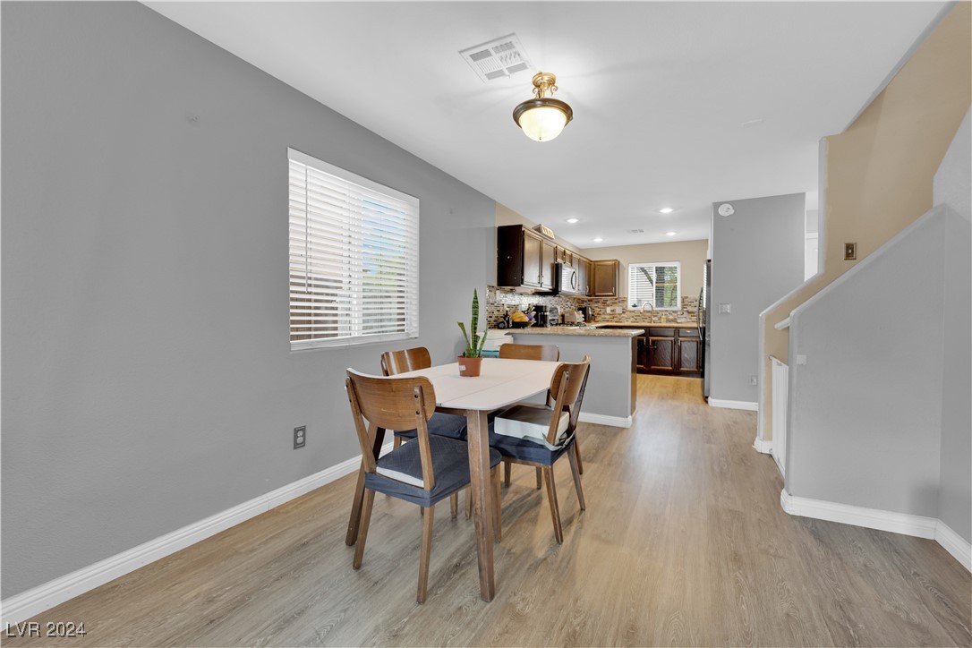 Dining area with a white table and wooden chairs opening into a kitchen with dark cabinets.