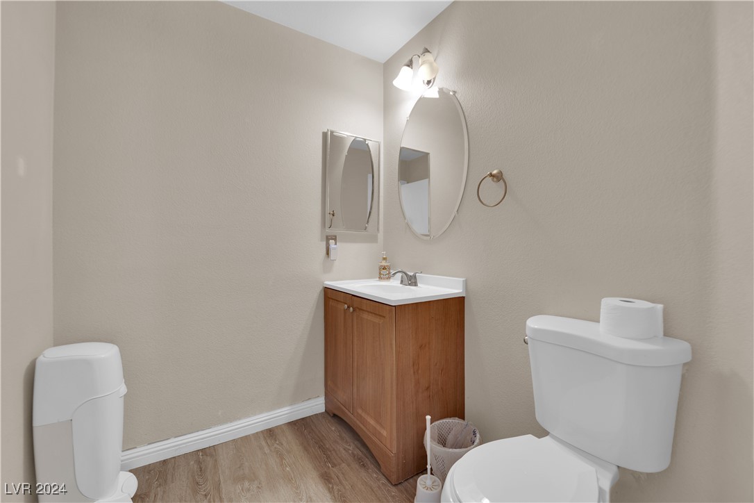 Bathroom with a wood vanity, oval mirror, and wood-look flooring.
