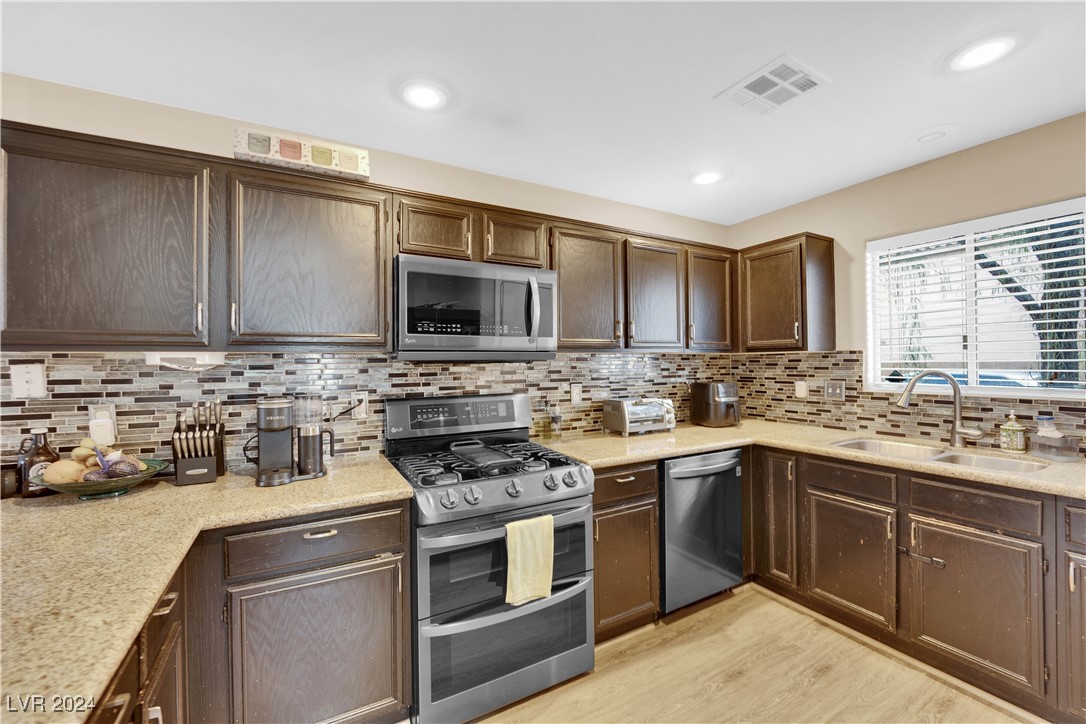 Kitchen with dark wood cabinets, tiled backsplash, stainless steel appliances, and a window above the sink.