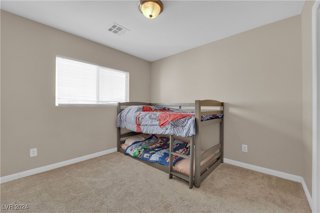 Bedroom with a gray bunk bed, colorful bedding, beige walls, and a window with blinds.