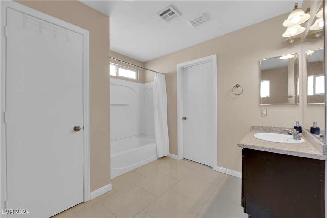Bathroom with a white tub and shower, tiled floor, and dark vanity with an oval sink.