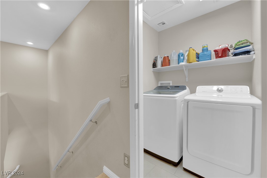 Laundry room with a washer and dryer beneath a shelf of supplies, viewed beside the stairway.