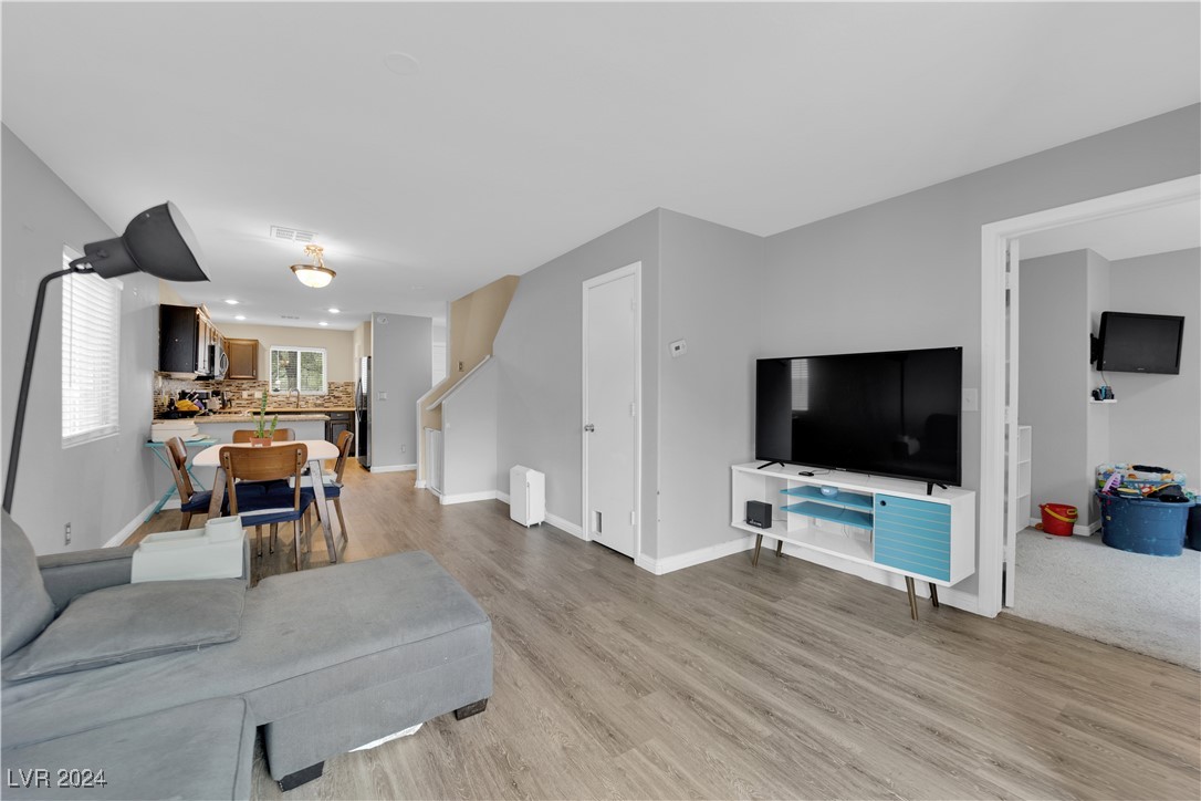 Open-plan living room with a gray sectional, television, dining area, and kitchen beyond.