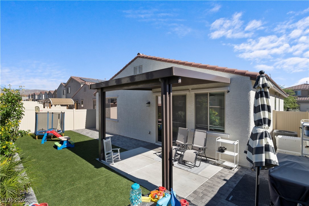 Fenced backyard with covered patio, artificial turf, outdoor seating, and children's play equipment.