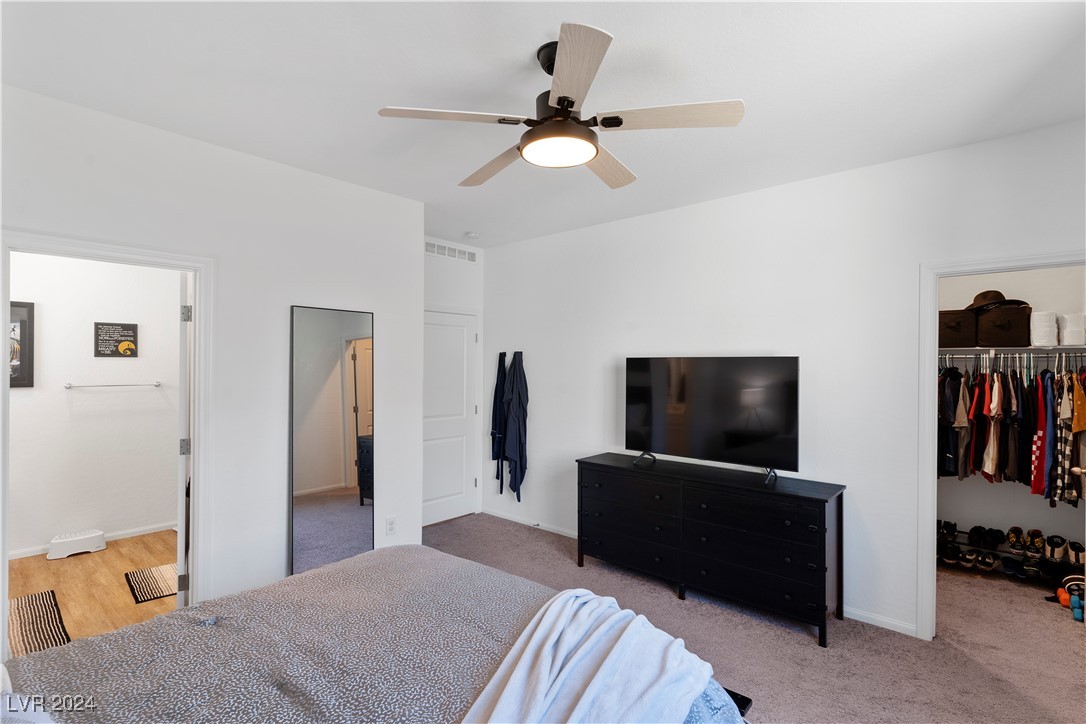 Bedroom with a black dresser and television, ceiling fan, and open walk-in closet.