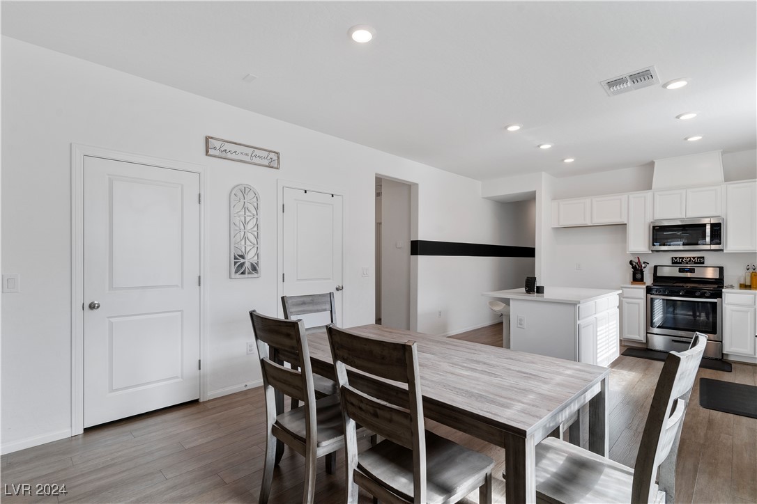 Dining table and dark chairs beside a bright white kitchen with a stainless steel range.