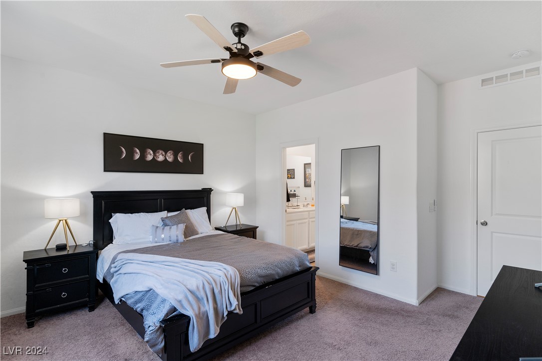 Furnished bedroom with black bed frame, ceiling fan, and doorway to an adjoining bathroom.