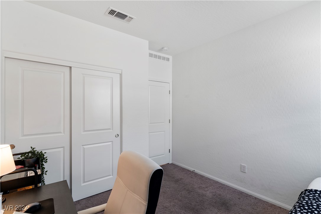 Bedroom with paneled closet doors, gray carpet, a desk and chair, and the edge of a bed.