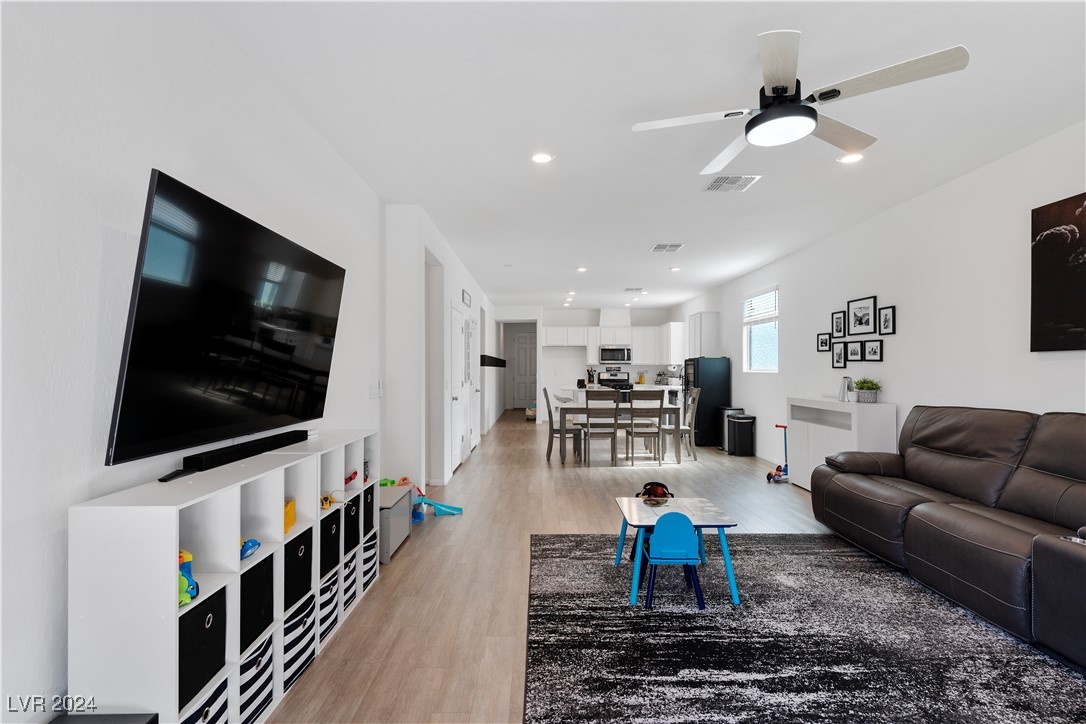 Open-plan living room with a dark leather sectional, wall-mounted television, and dining area beyond.
