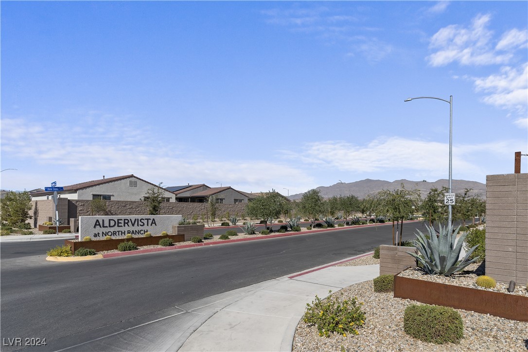 Aldervista at North Ranch entrance sign beside a landscaped street, with homes and mountains beyond.