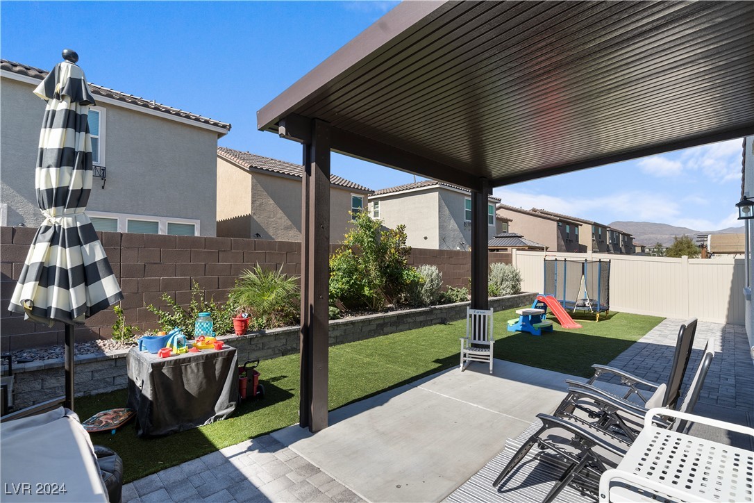 Backyard patio beneath a covered pergola, with artificial turf, outdoor seating, and a children's play area.