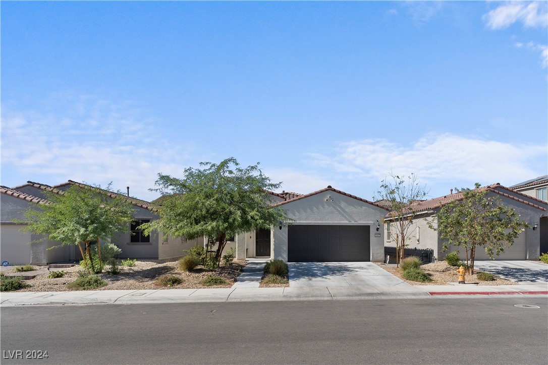 Single-story stucco home with a dark garage, tiled roof, and desert landscaping.