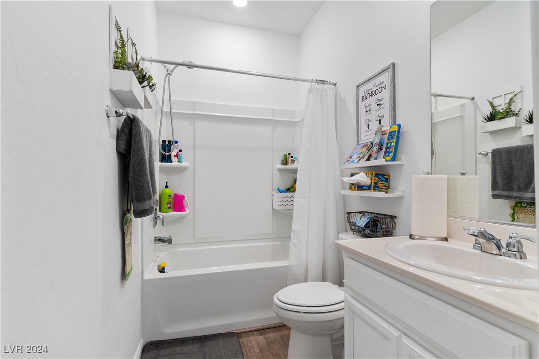 Bathroom with a white tub and shower curtain, toilet, and vanity with a large mirror.
