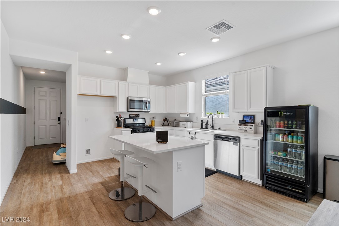 White kitchen with a large island, two stools, stainless steel appliances, and a glass-front beverage refrigerator.