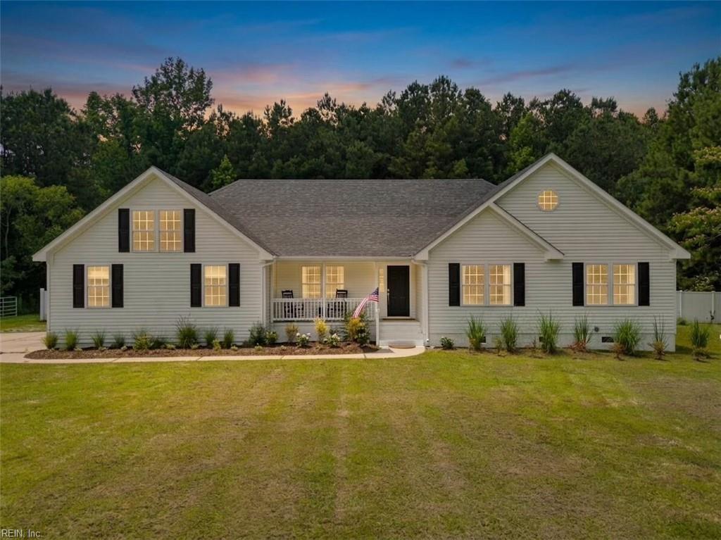 Light-gray gabled house with black shutters, a covered porch, and a broad lawn at dusk.