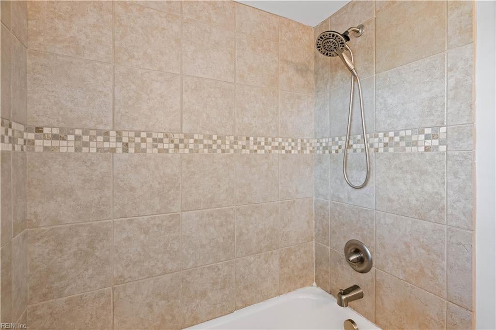 Tub and shower with beige tile, a mosaic accent strip, and handheld showerhead.