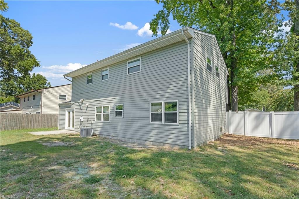 Two-story gray-sided house with a white privacy fence and patchy backyard lawn.