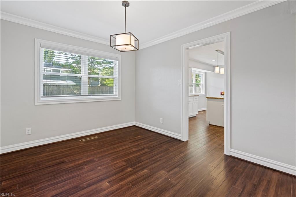 Empty dining room with dark wood floors, a large window, and an open doorway to the kitchen.