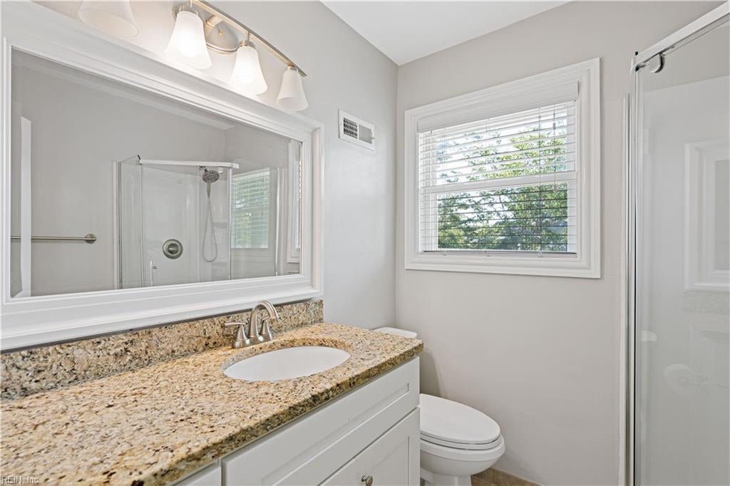 Bathroom with granite vanity, large mirror, glass-enclosed shower, and a window with blinds.