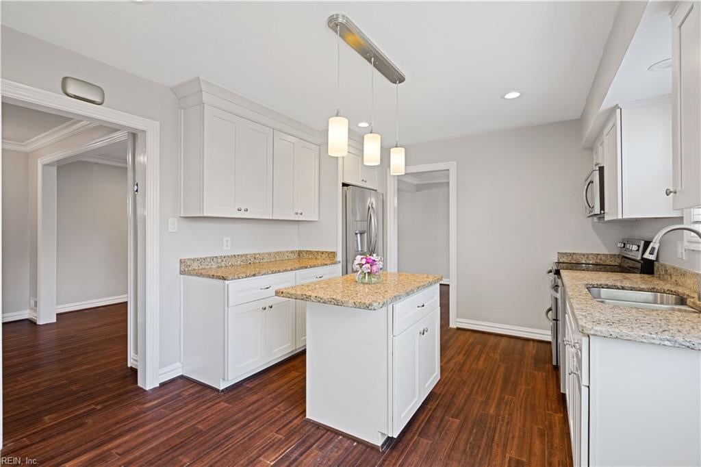 Kitchen with white cabinets, granite counters, central island, stainless steel refrigerator, and dark wood floors.