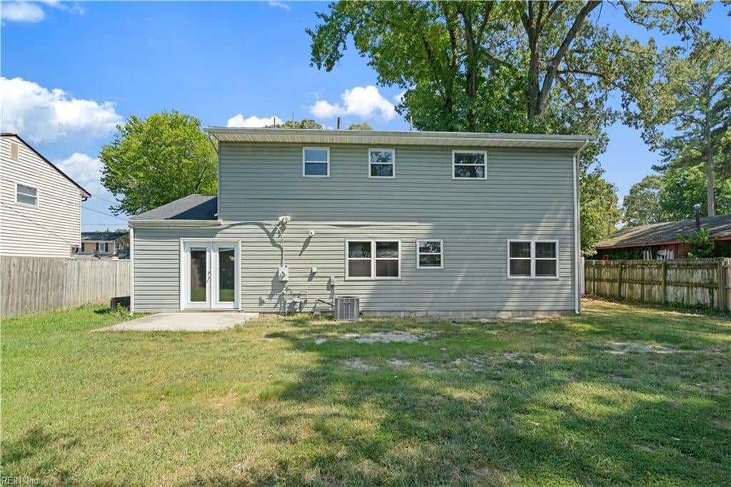 Rear of a two-story gray home with a fenced lawn and mature trees.
