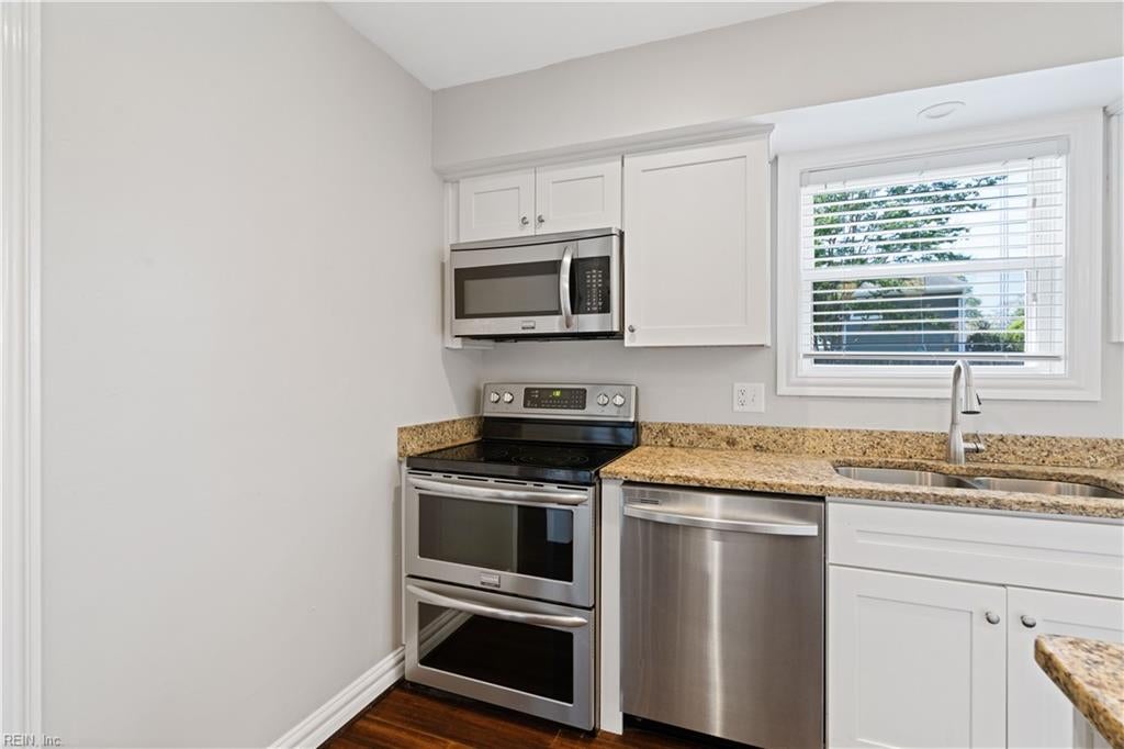 Kitchen with white cabinets, granite counters, stainless steel appliances, and a window above the sink.