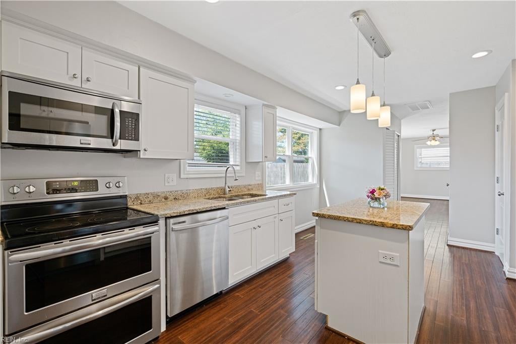 Bright kitchen with white cabinets, stainless steel appliances, granite counters, and a central island.