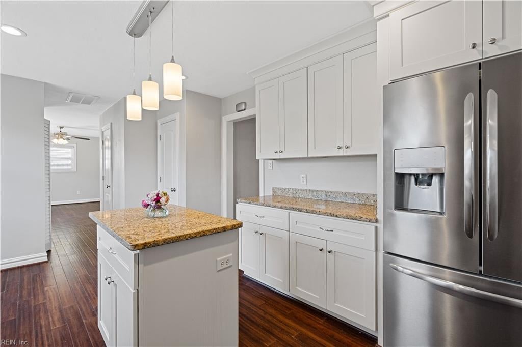 Kitchen with white shaker cabinets, granite island, stainless steel refrigerator, and dark wood floors.