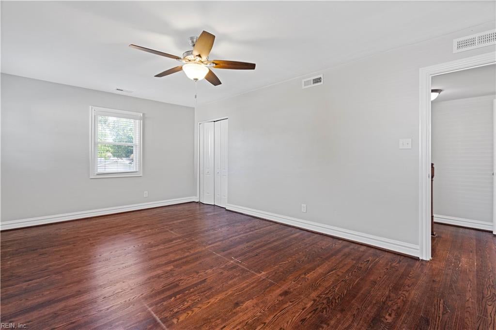Empty bedroom with dark hardwood floors, a ceiling fan, a window, and a double-door closet.