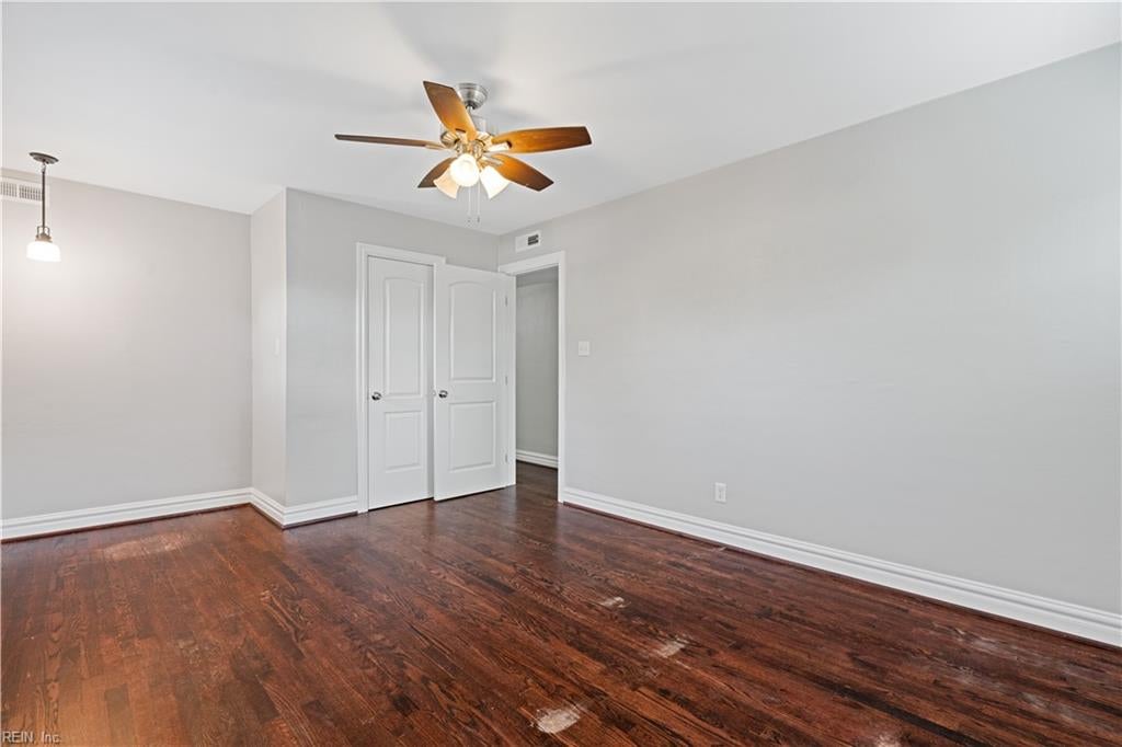 Empty room with dark hardwood floors, a ceiling fan, and open double closet doors.
