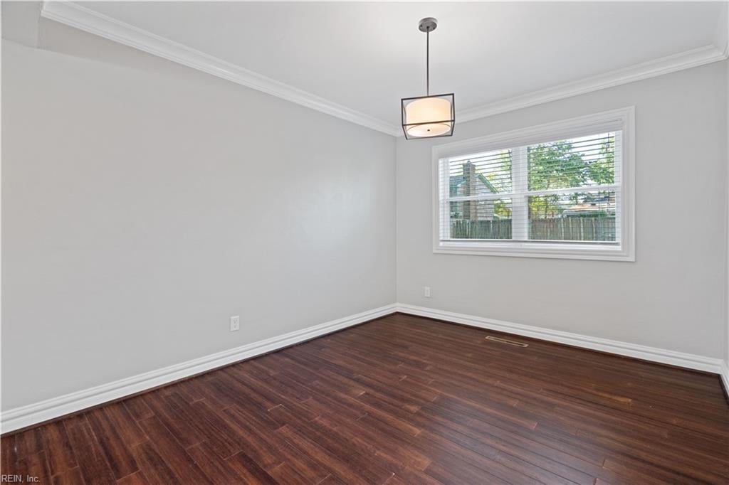 Empty room with dark hardwood floors, gray walls, white crown molding, and a wide window.