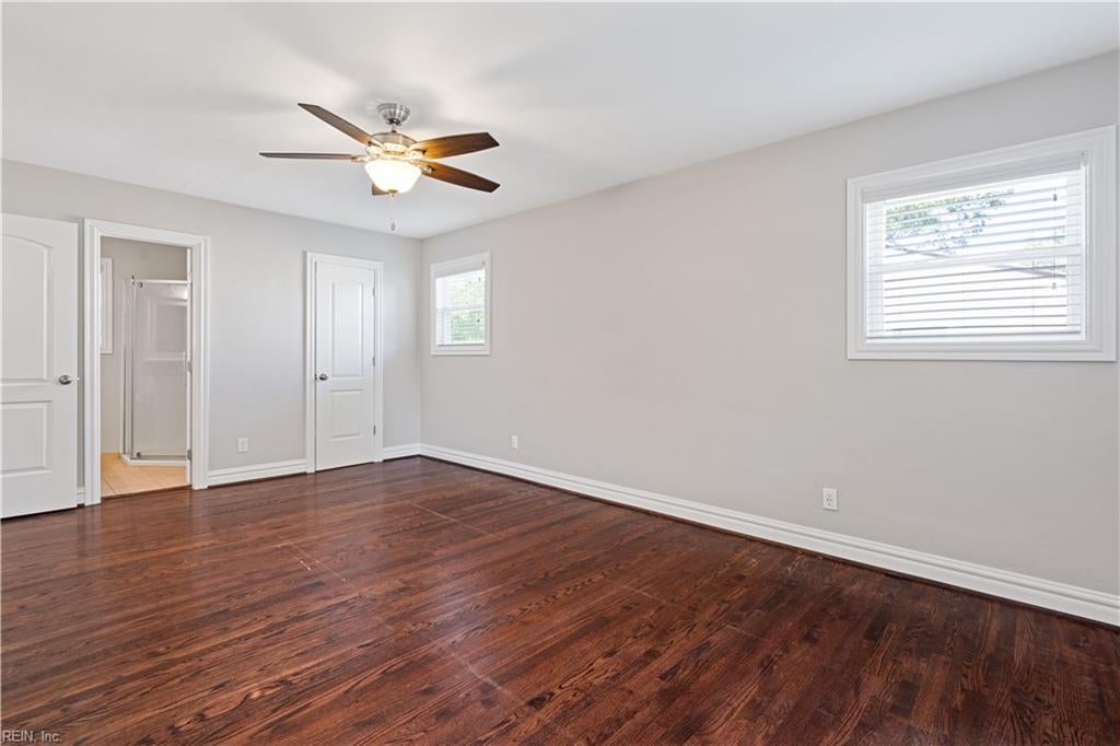 Empty bedroom with dark hardwood floors, a ceiling fan, and a doorway to a tiled bathroom.