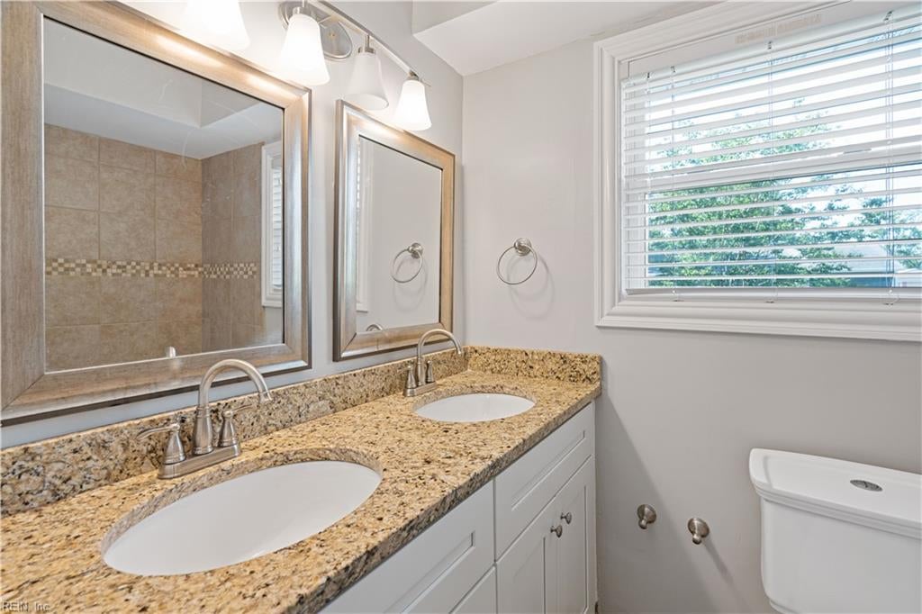 Bathroom with a granite double-sink vanity, framed mirrors, and a window with blinds.