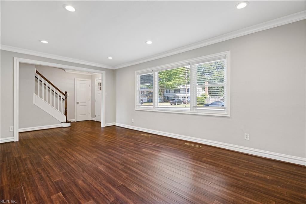 Vacant living room with dark wood floors, a wide window, and a staircase.