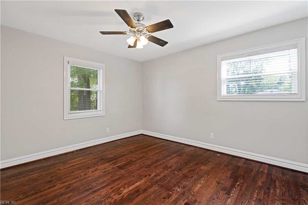 Empty bedroom with dark hardwood floors, two windows, and a ceiling fan with light.
