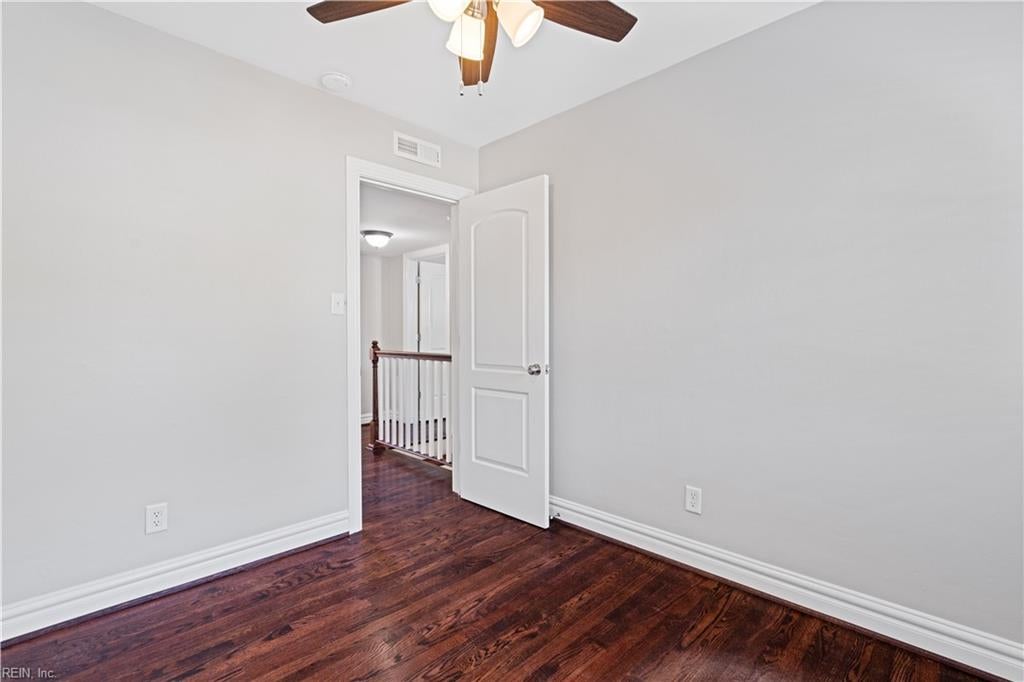 Empty bedroom with dark hardwood floors, a ceiling fan, and an open door to a hallway.