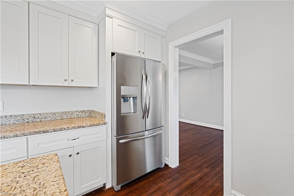 Kitchen with white cabinetry, granite counters, and a stainless steel refrigerator beside a doorway.