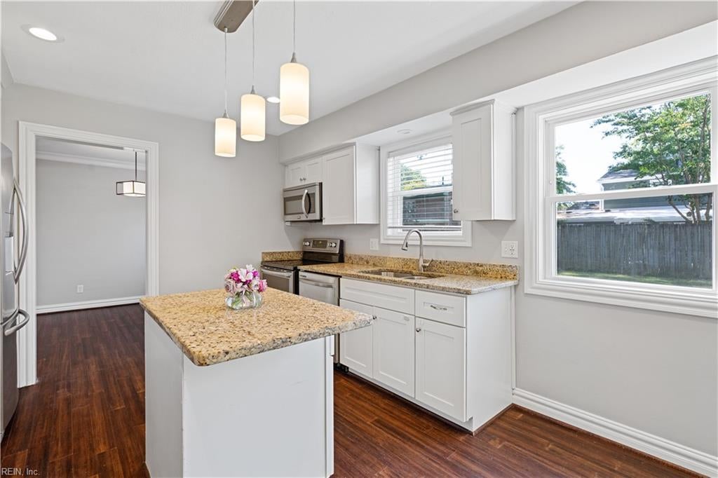 Bright kitchen with a granite-topped island, white cabinets, stainless steel appliances, and large windows.