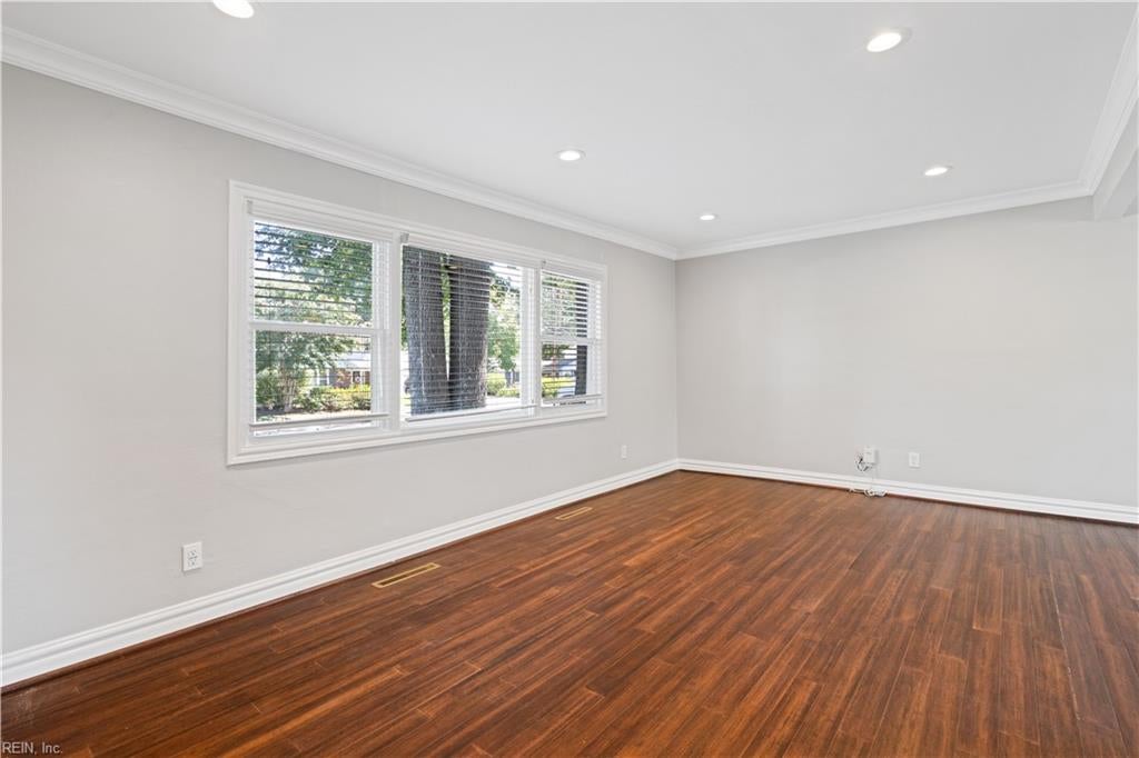 Empty room with reddish-brown hardwood floors and wide windows with blinds.
