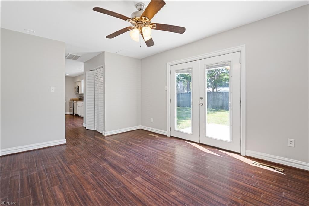 Empty living room with dark hardwood floors, ceiling fan, and glass doors to the backyard.