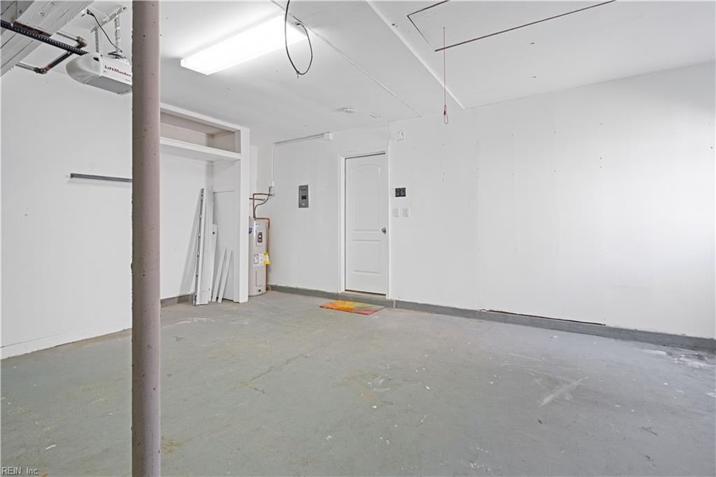 Empty garage with a concrete floor, overhead door opener, water heater, and small back door.